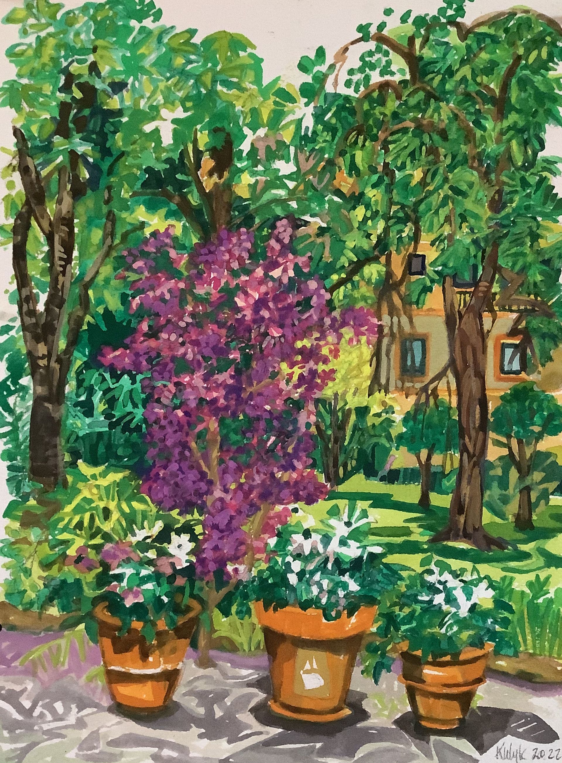 ©Karen Kulyk - Potted flowers in a garden with a blooming purple tree, greenery, and a building in the background.