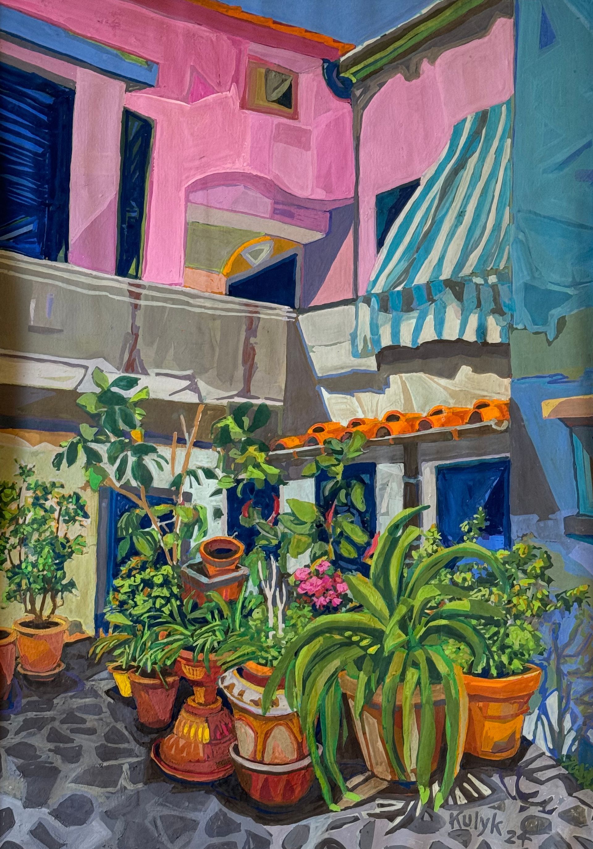 ©Karen Kulyk - Colorful courtyard with potted plants, pink and blue buildings, and a striped awning.