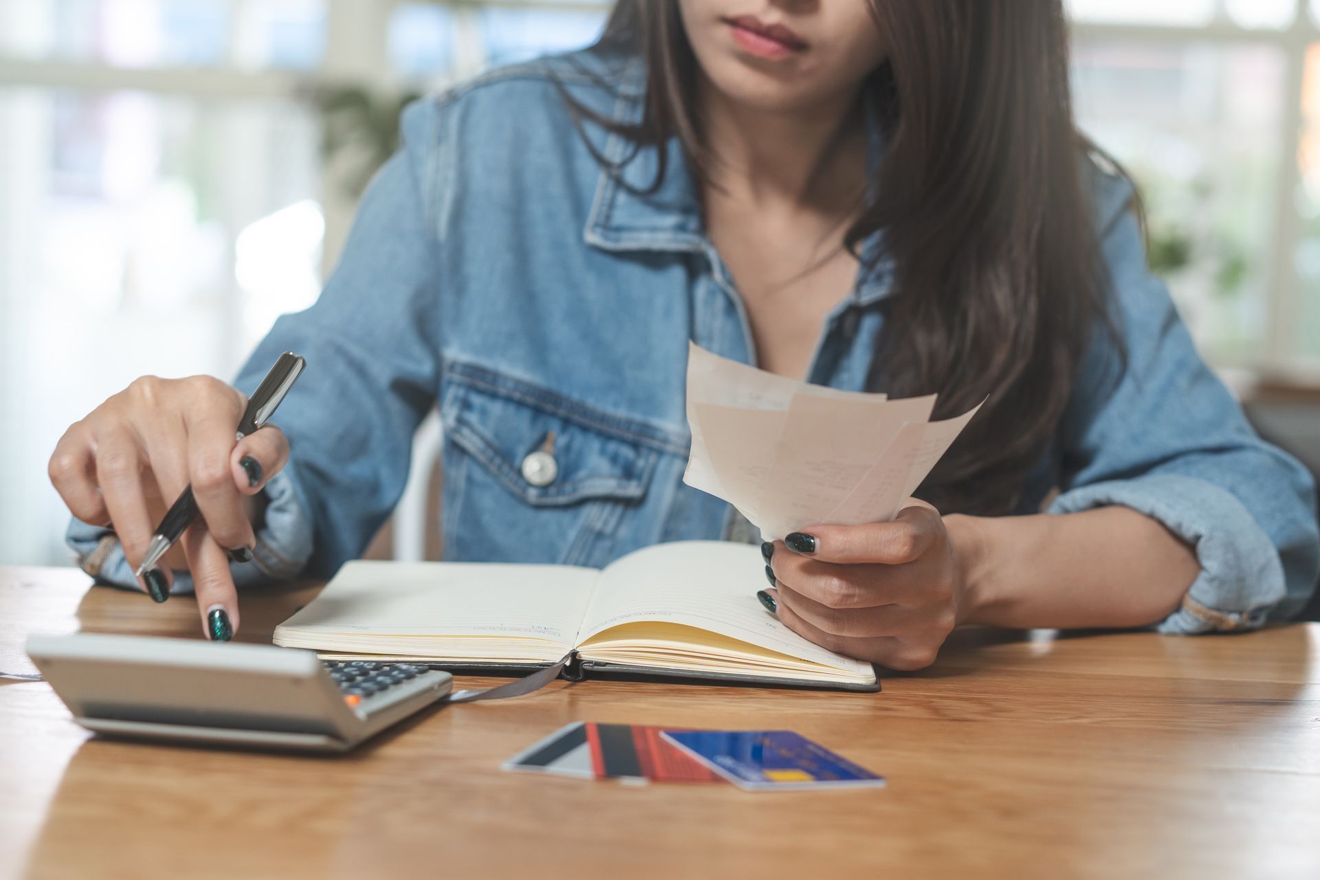 A woman uses a acalculator while holding a piece of paper and a notebook while sitting.