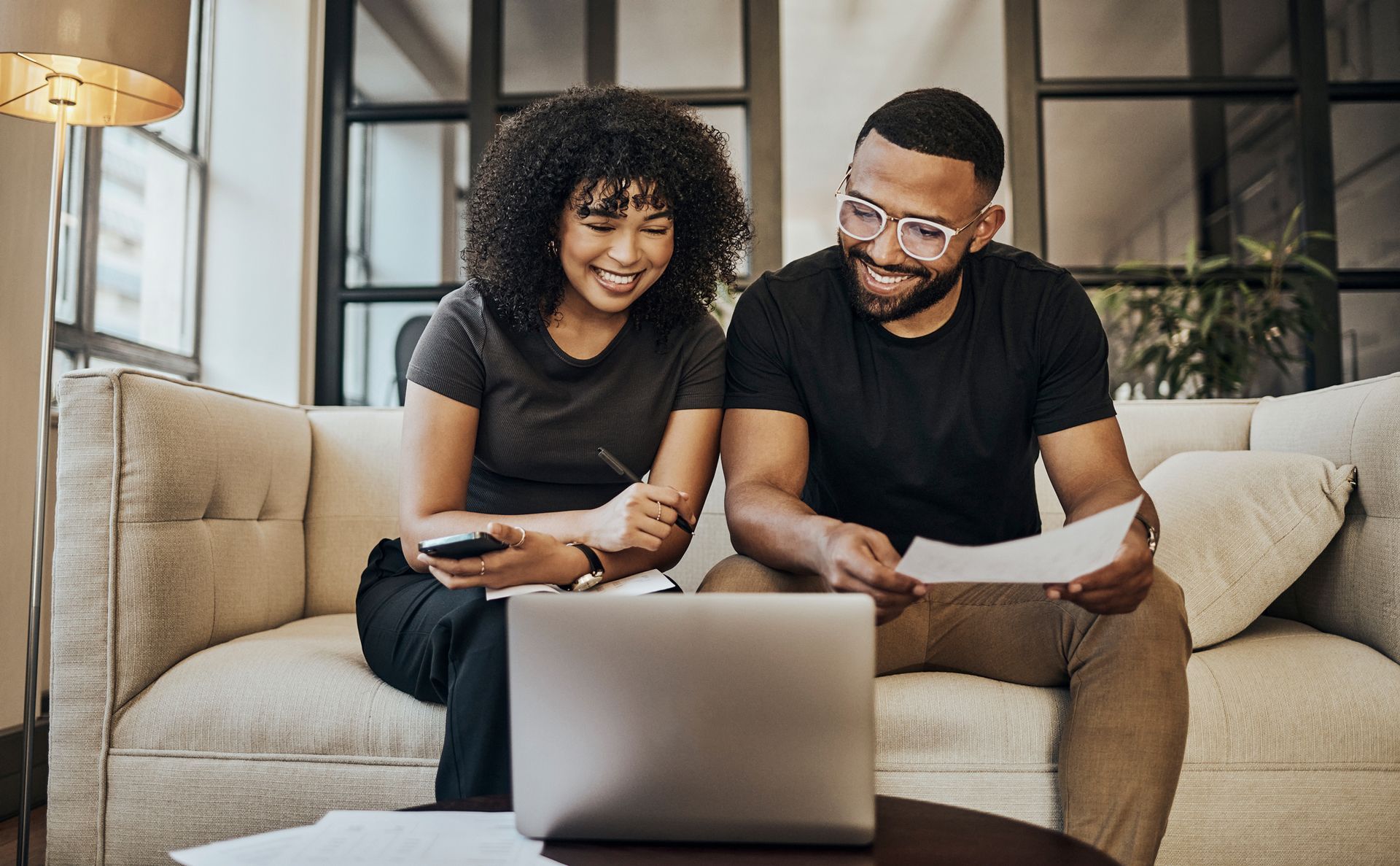 A smiling couple is seated on their coach, reviewing in their laptop their personal loan. A smiling couple is seated on their coach, reviewing in their laptop their personal loan.
