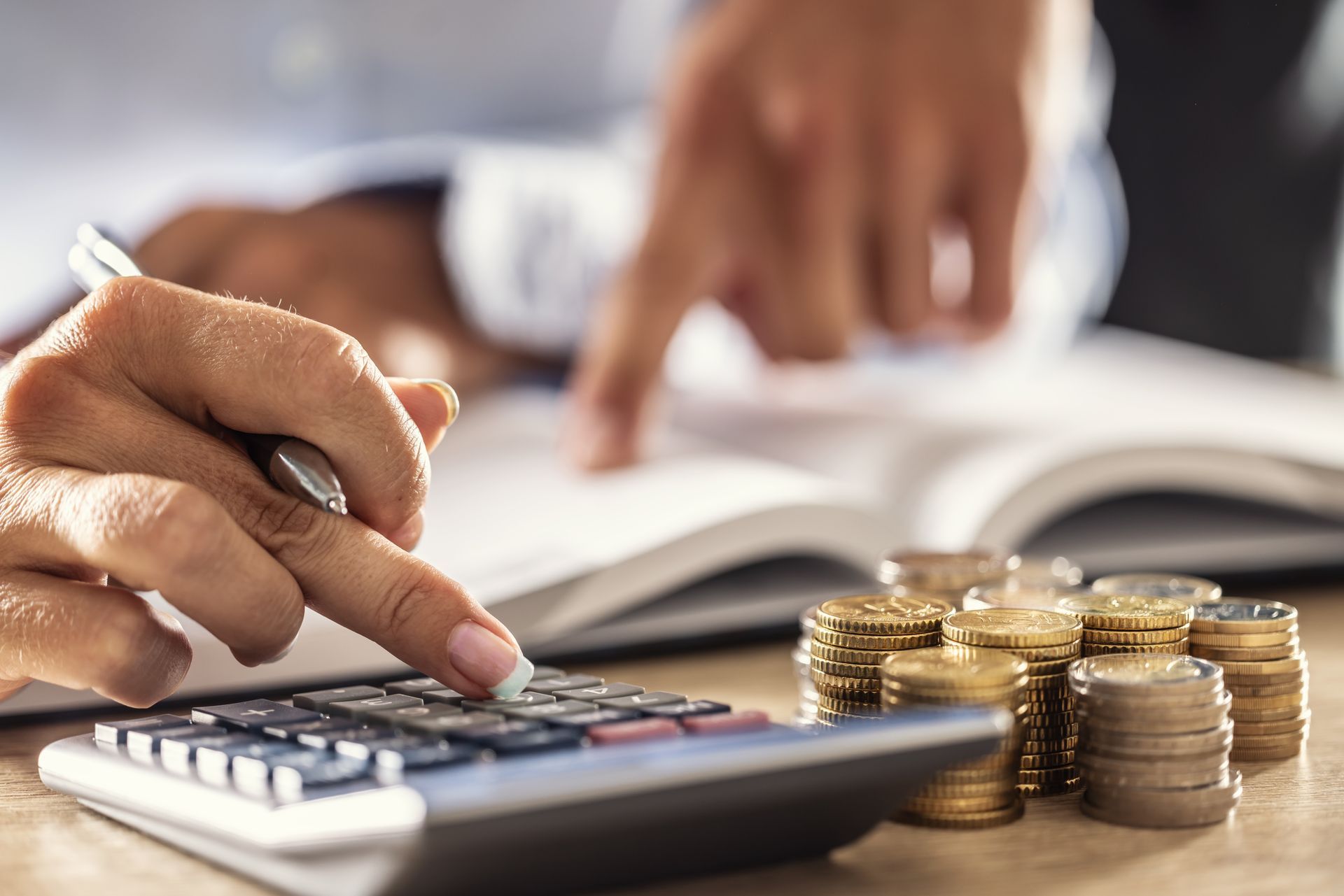 Close-up of a woman’s hands as it points at a calculator with a stack of coins next to it.