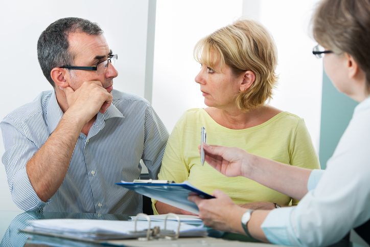 Woman and man talk while woman hands them a file, representing applying for personal loans.