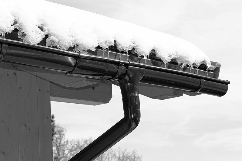 Une photo en noir et blanc d’une gouttière sur un toit recouvert de neige.