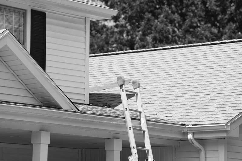 Une personne se tient debout sur une échelle sur le toit d’une maison.