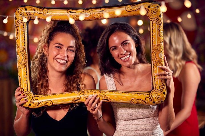 Two women smiling through a large vintage gold picture frame prop.