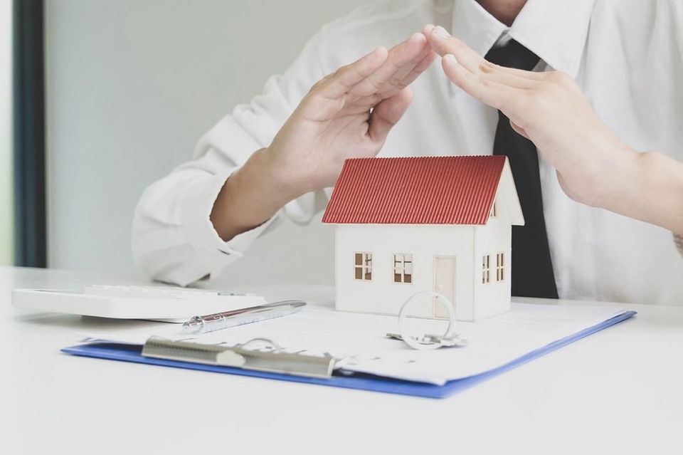 A man is sitting at a table with a model house on a clipboard.