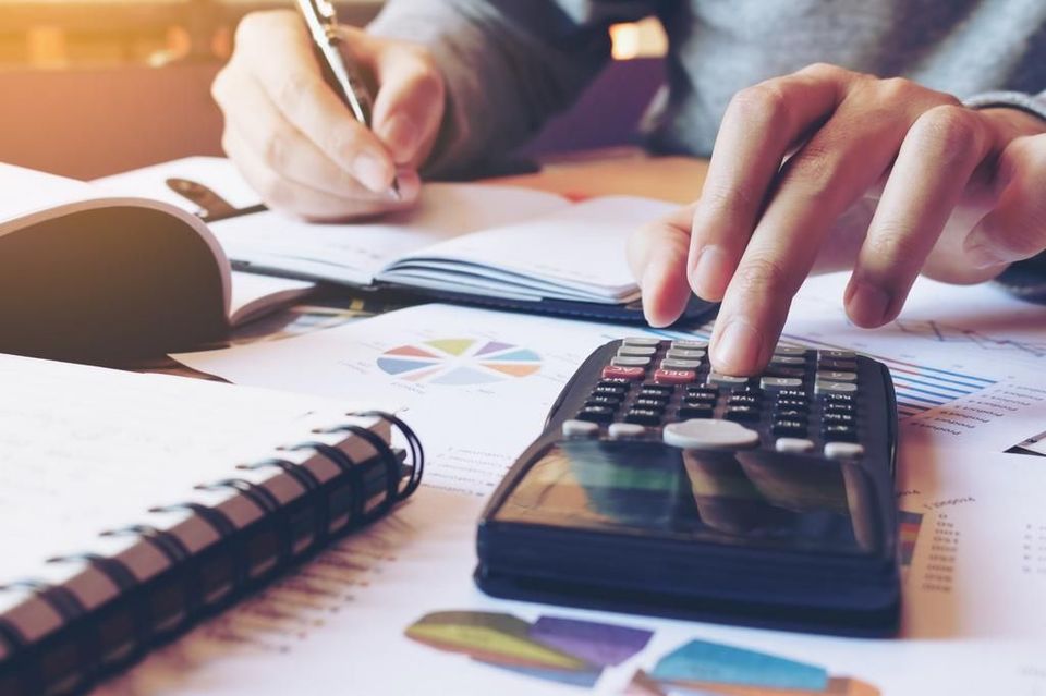 A person is using a calculator while writing in a notebook.