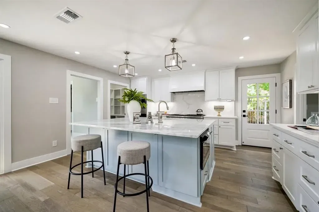 Bright modern kitchen with white cabinets, blue island, bar stools, and pendant lights