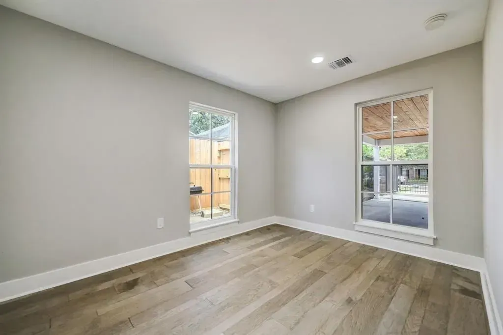 Empty modern room with gray walls, wood floor, and two tall windows.