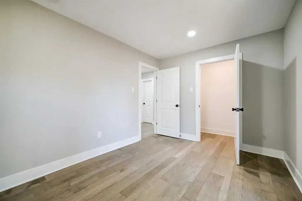 Empty light-gray bedroom with wood floors and an open white door.