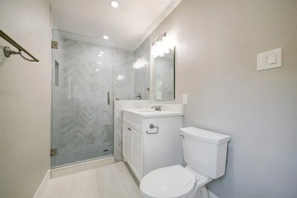 Small modern bathroom with glass shower, white vanity, toilet, and gray walls