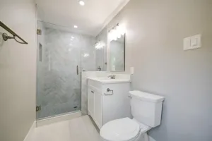 Modern gray bathroom with glass shower, white vanity, toilet, and mirror