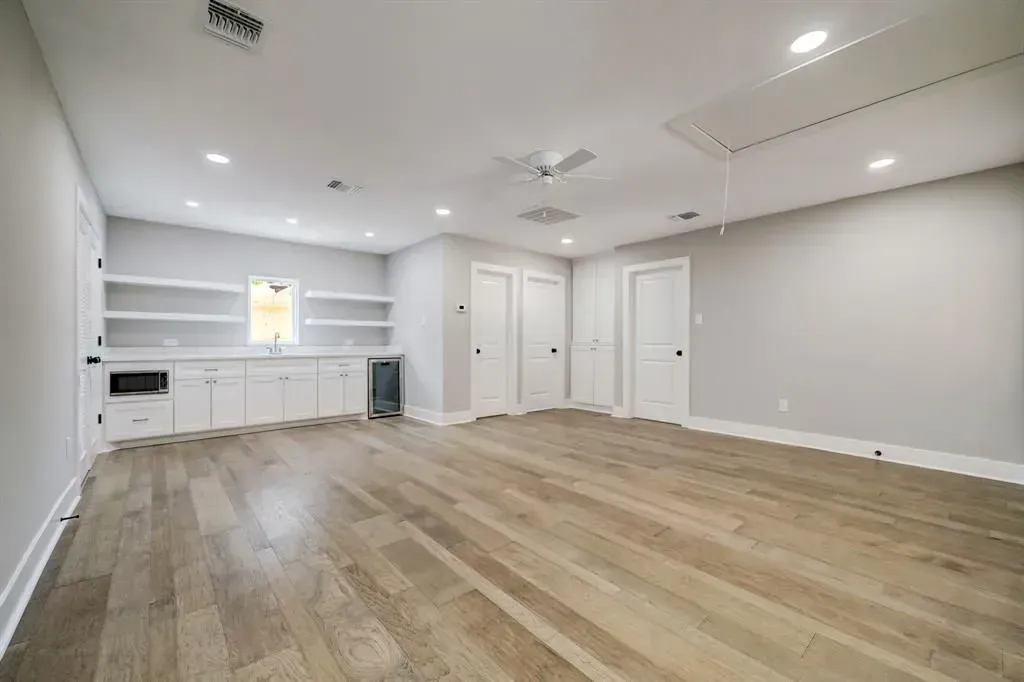 Empty modern room with light wood floors, white walls, built-in shelves, and recessed ceiling lights