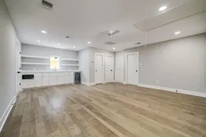 Empty modern room with light wood floors, white built-ins, and recessed ceiling lights.