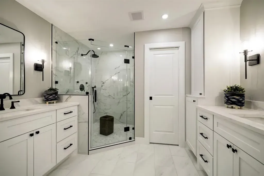 Bright white modern bathroom with glass shower, double vanities, and black fixtures