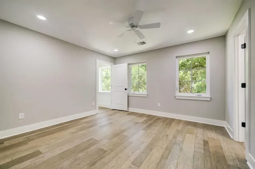 Empty modern room with light wood floors, gray walls, and three windows under recessed ceiling lights.