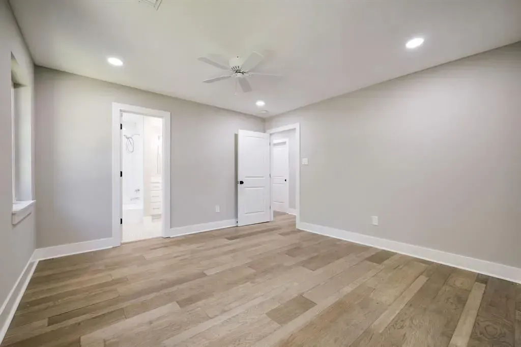 Empty modern room with light wood floors, white walls, recessed lights, and two doorways.
