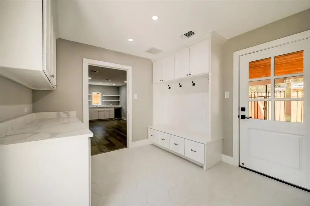 Bright white entryway with built-in cabinets, pendant lights, and a glass door with orange curtains