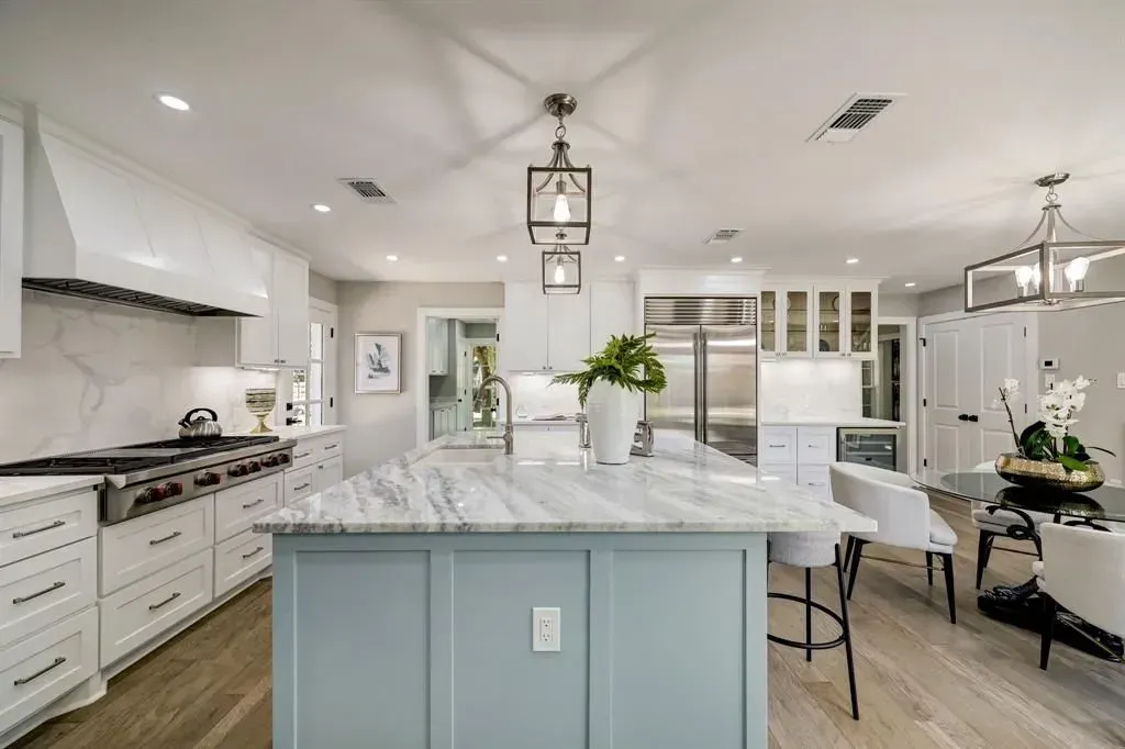 Bright, modern kitchen with marble island, white cabinets, pendant lights, and dining area.