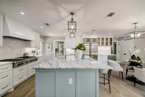 Bright modern kitchen with marble island, white cabinets, and dining area in the background