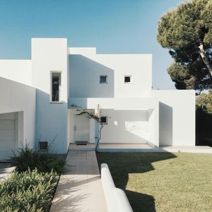Modern white house with a walkway, lawn, and trees under a clear blue sky