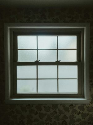 Dim window with six frosted panes above patterned wallpaper indoors