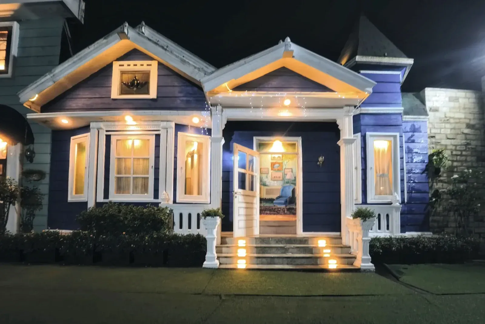 Blue house with lit porch and steps at night, decorated with warm white lights.