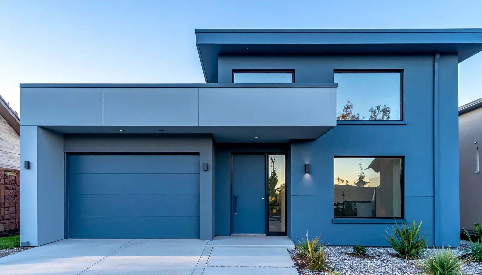 Modern blue two-story house with a garage, large windows, and a front driveway