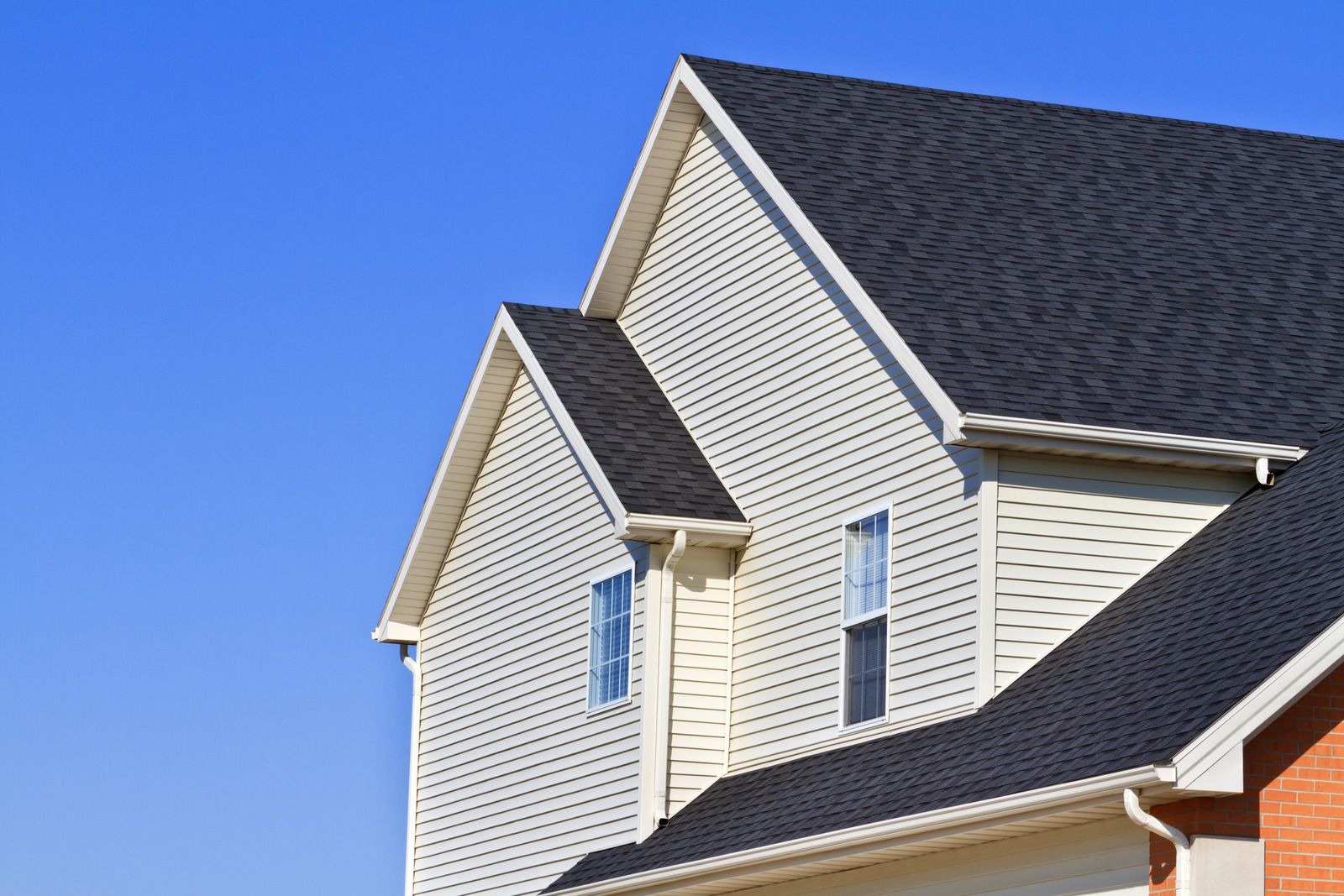 Suburban house roof and siding against a clear blue sky