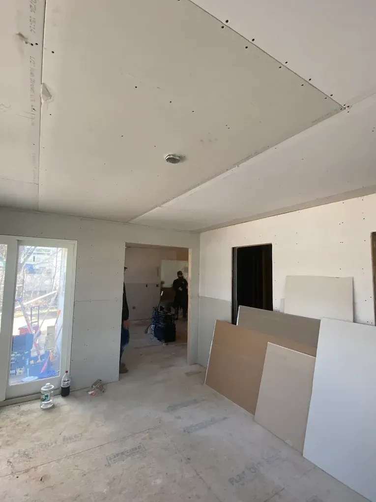 Interior room under construction, drywall installed on ceiling and walls. Construction materials on the floor.