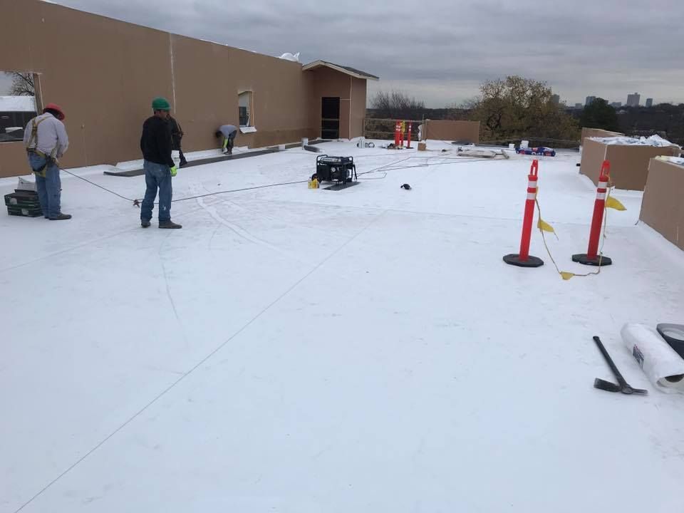 House with roof being repaired; red brick, green shingles, workers, ladder, cloudy sky.