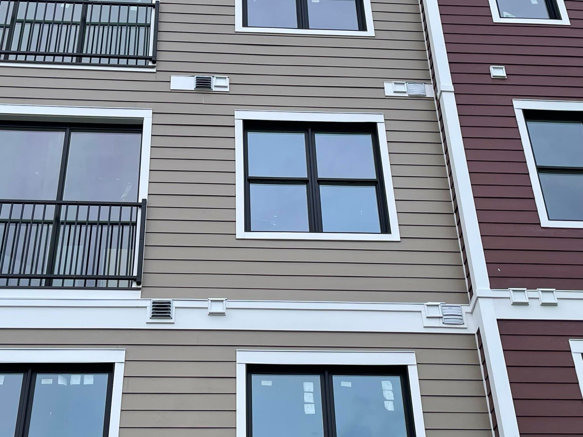 Building exterior with tan and burgundy siding, black-framed windows, and balconies.