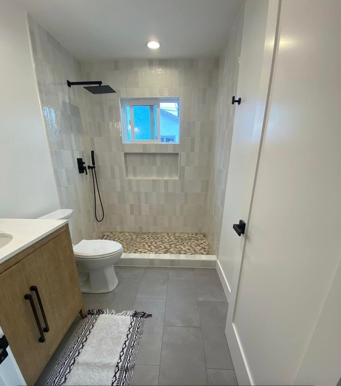 Bathroom with tiled shower, pebble floor, toilet, vanity, and gray floor.