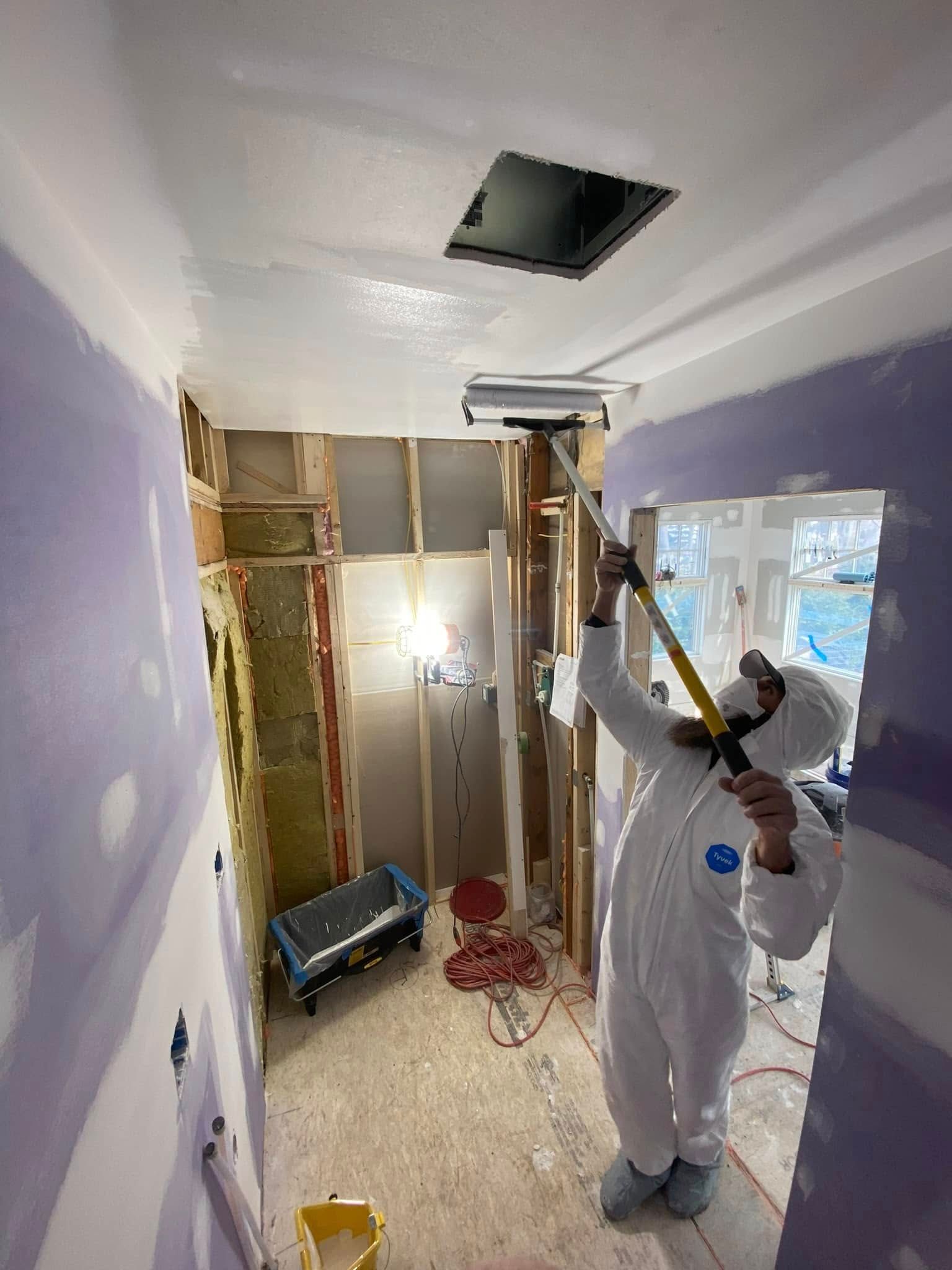 Person in a hazmat suit painting a ceiling in a room under construction.