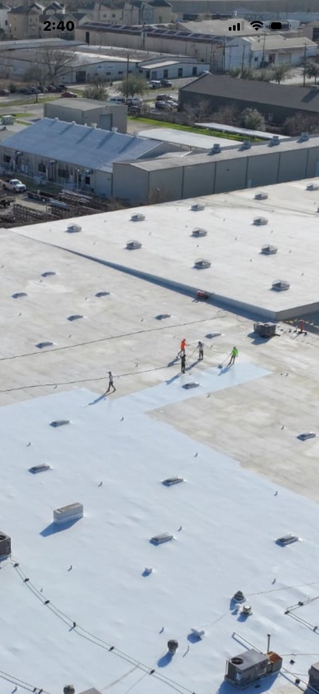 Aerial view of workers on a large, flat commercial roof, possibly under construction or repair.