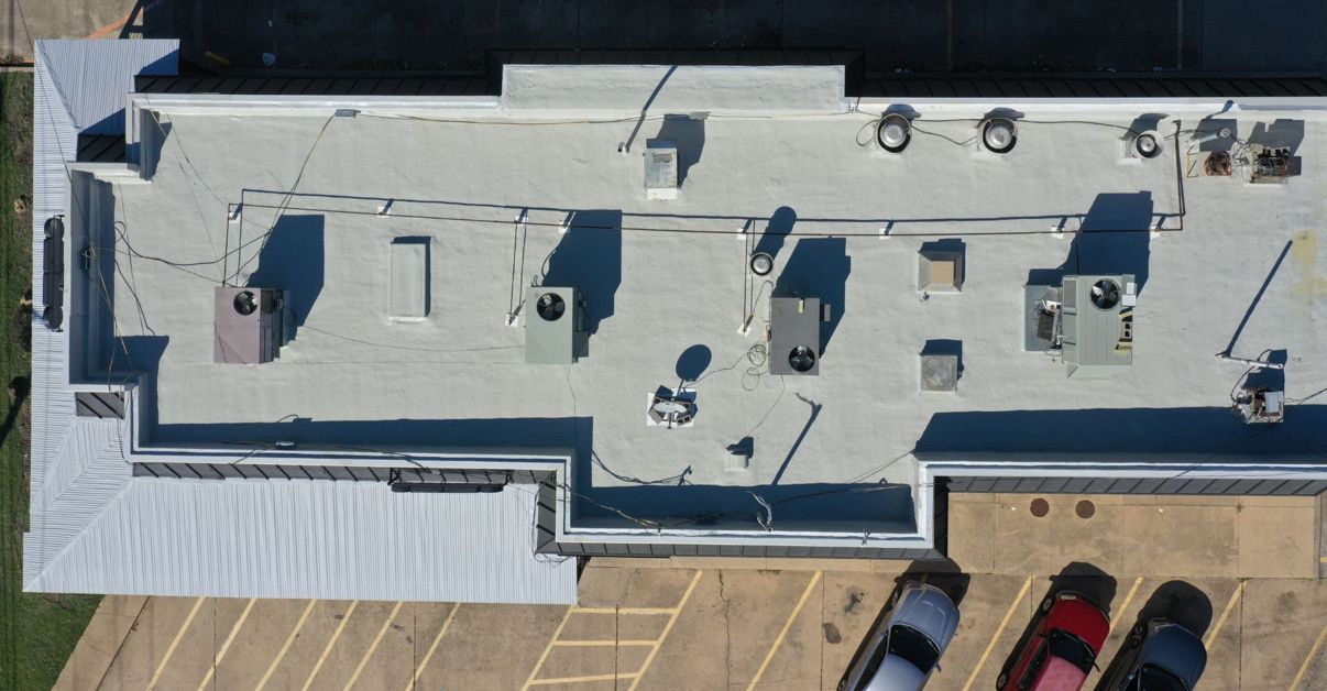 Overhead view of a building roof with HVAC units, vents, and piping. Cars are parked below.