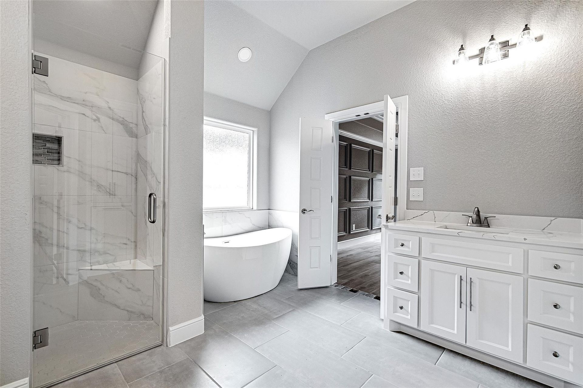 Bathroom with a glass shower, gray vanity, marble-like tile, and a large mirror.