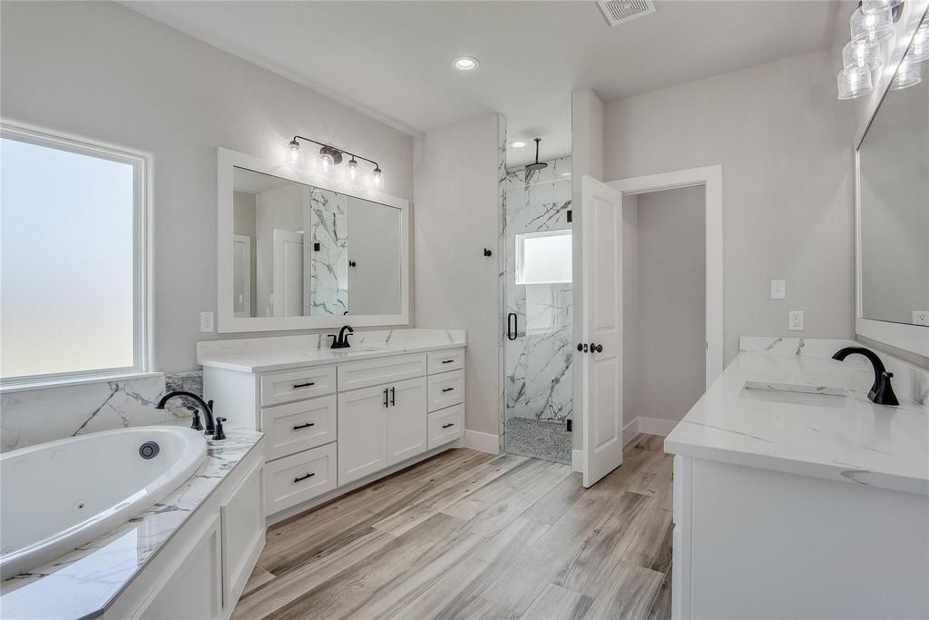 Modern bathroom with glass shower, white walls, wood floors, and dark vanity.