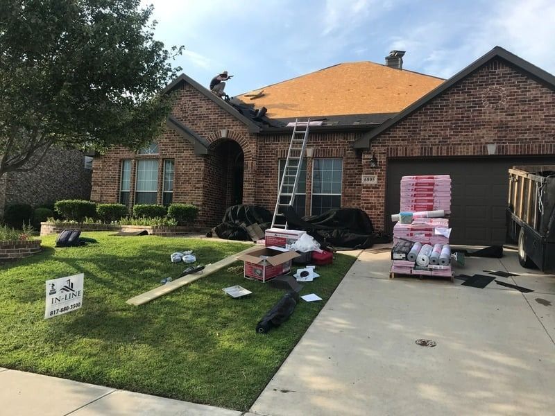 Roofers working on a brick house, materials scattered in the yard.