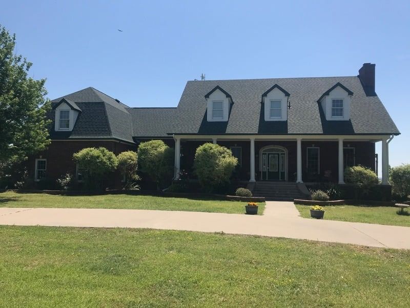 A brick house with white columns and a dark roof on a sunny day.