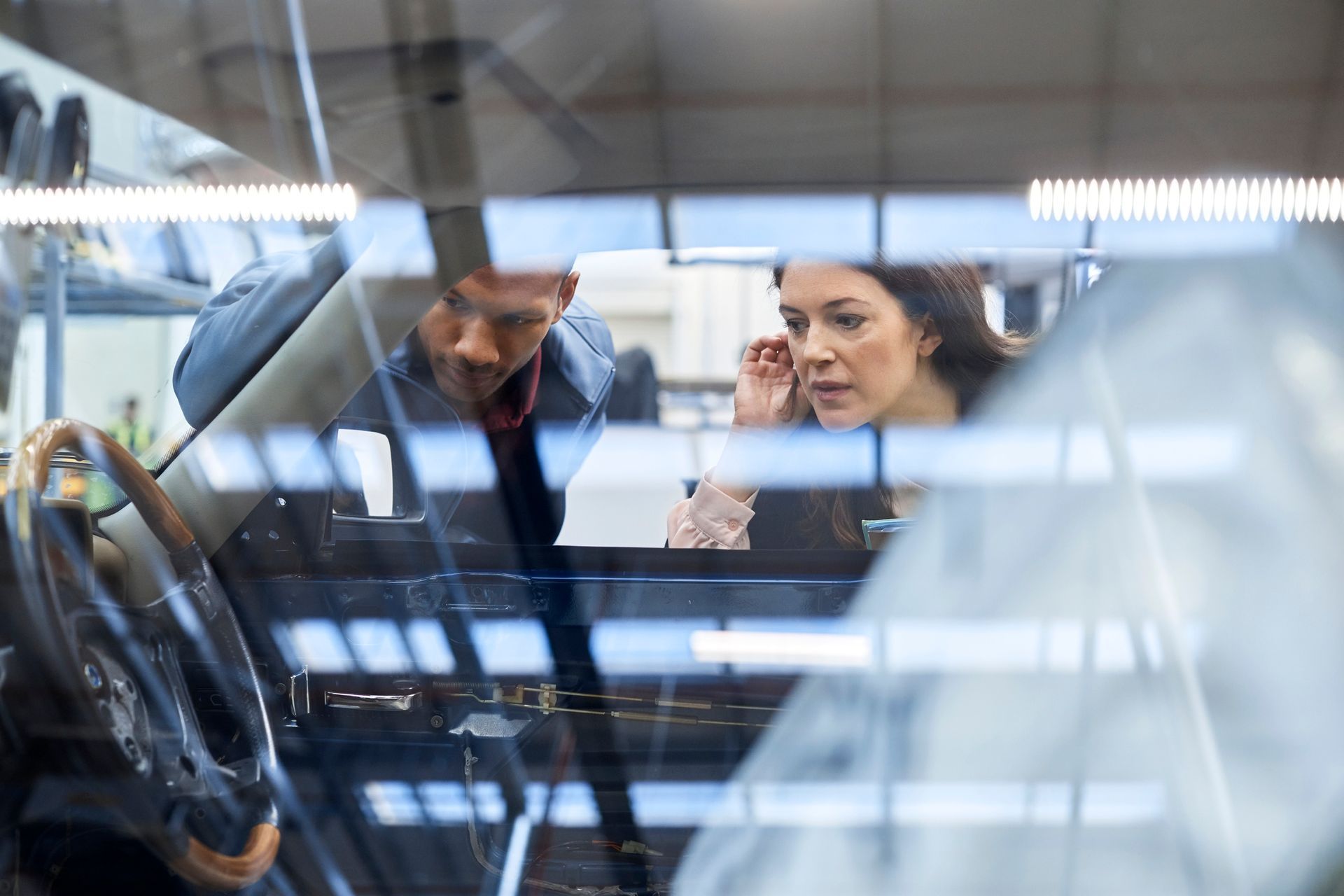 A man and a woman are looking at a car in a showroom.