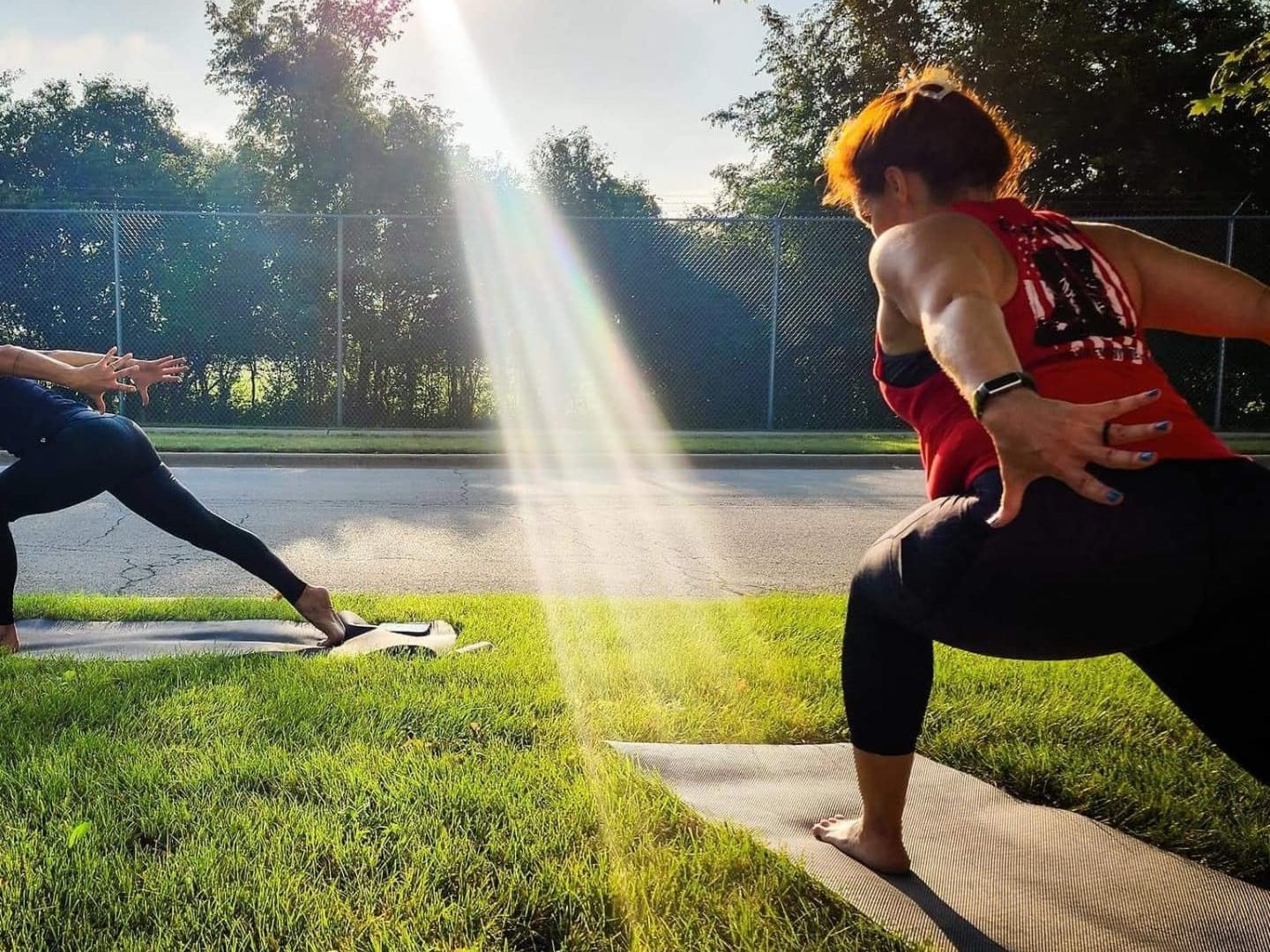 Two women are doing yoga in a park with the sun shining through the trees