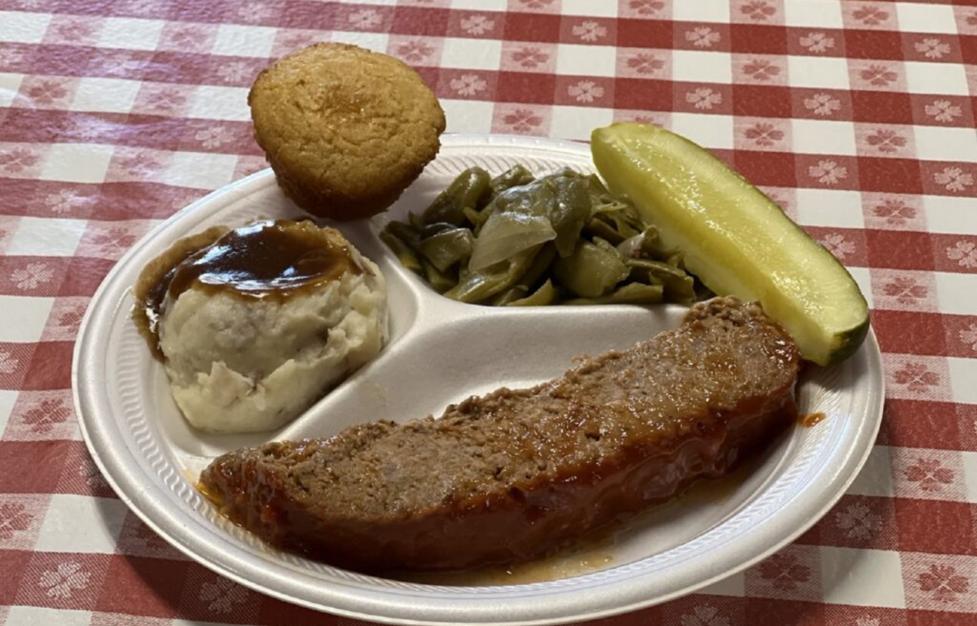 Plate with meatloaf, mashed potatoes, green beans, pickle, and cornbread.
