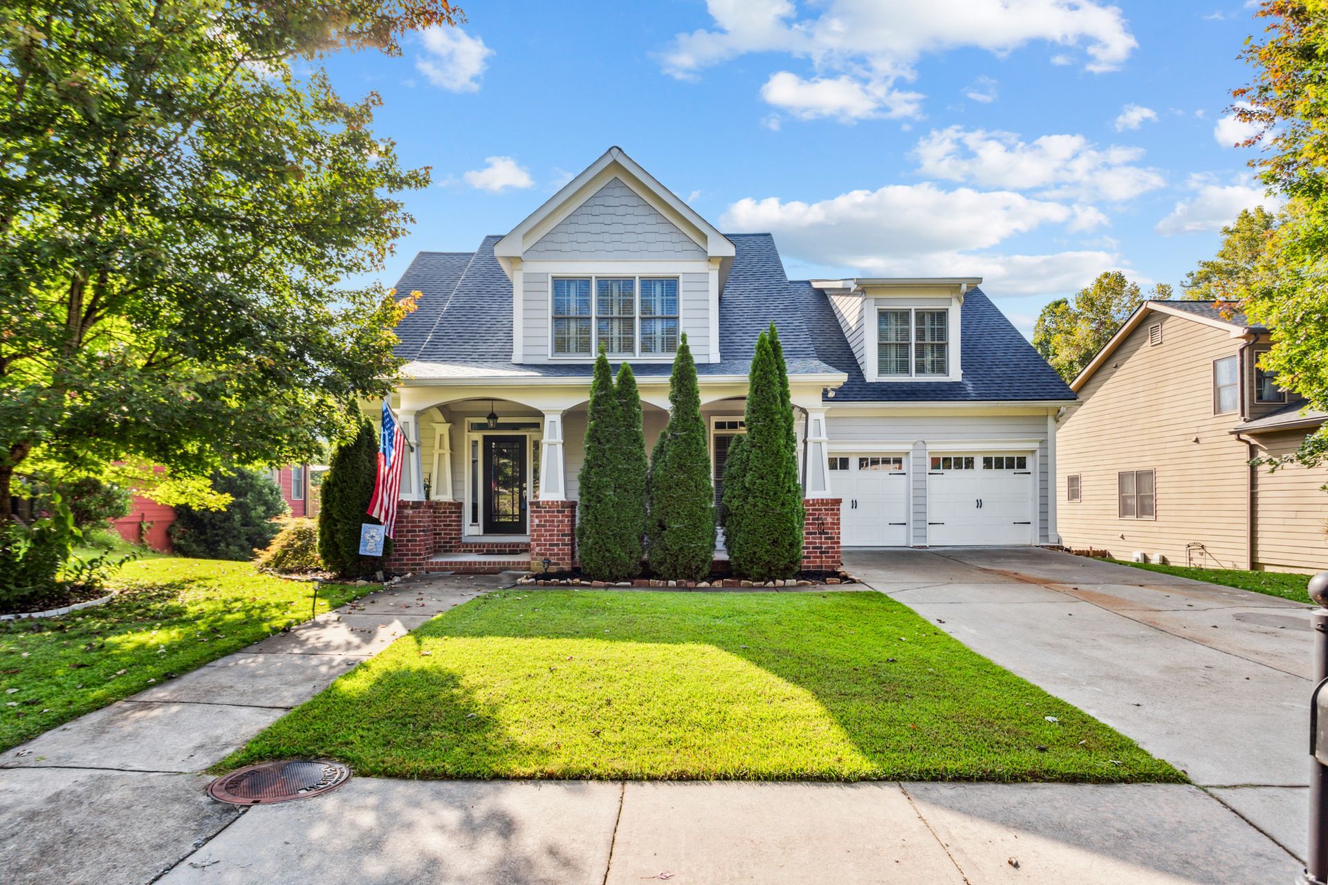 Suburban house with stone porch, two-car garage, and a green lawn on a sunny day