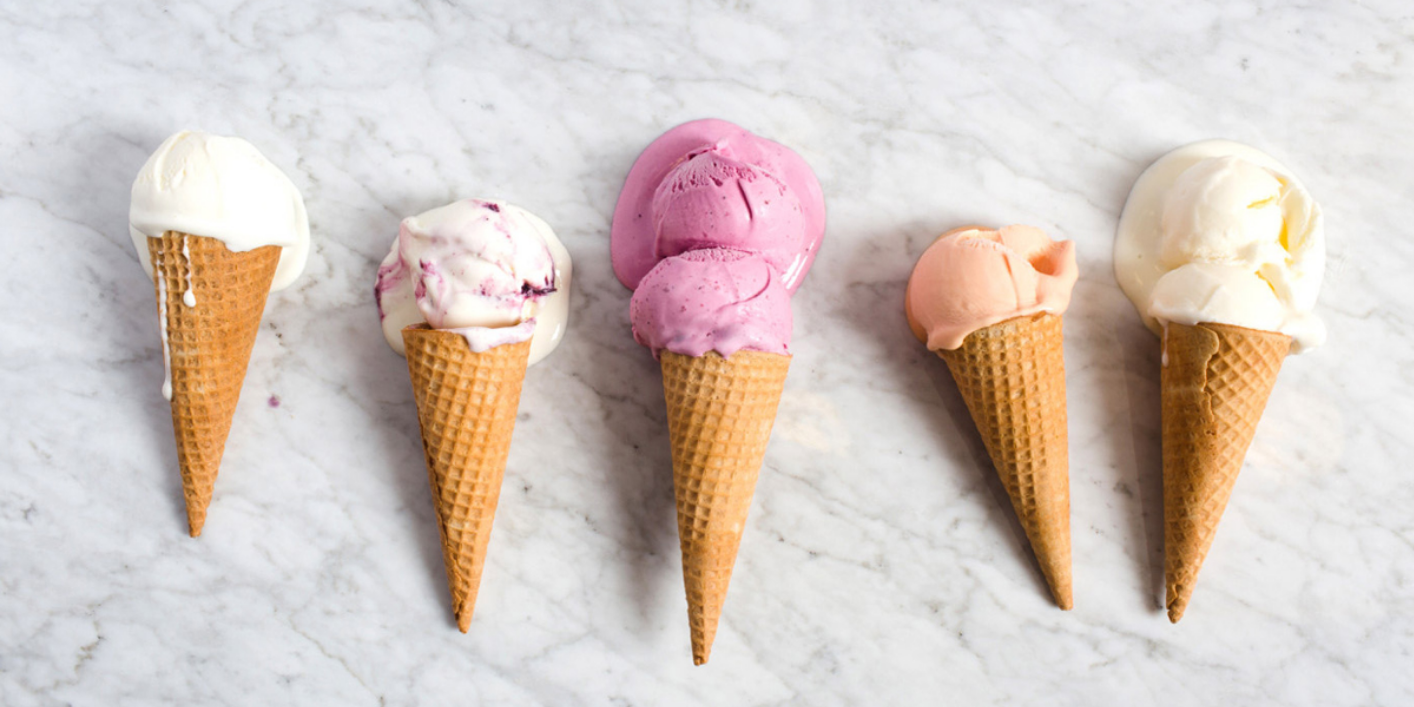 Five ice cream cones with different colored scoops on a white marble surface.