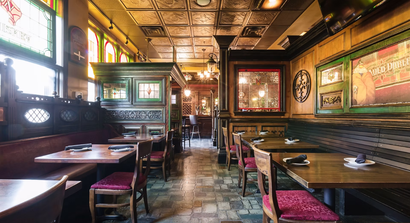 Interior of a pub with wooden tables, booths, and ornate decor. Dark, warm lighting.