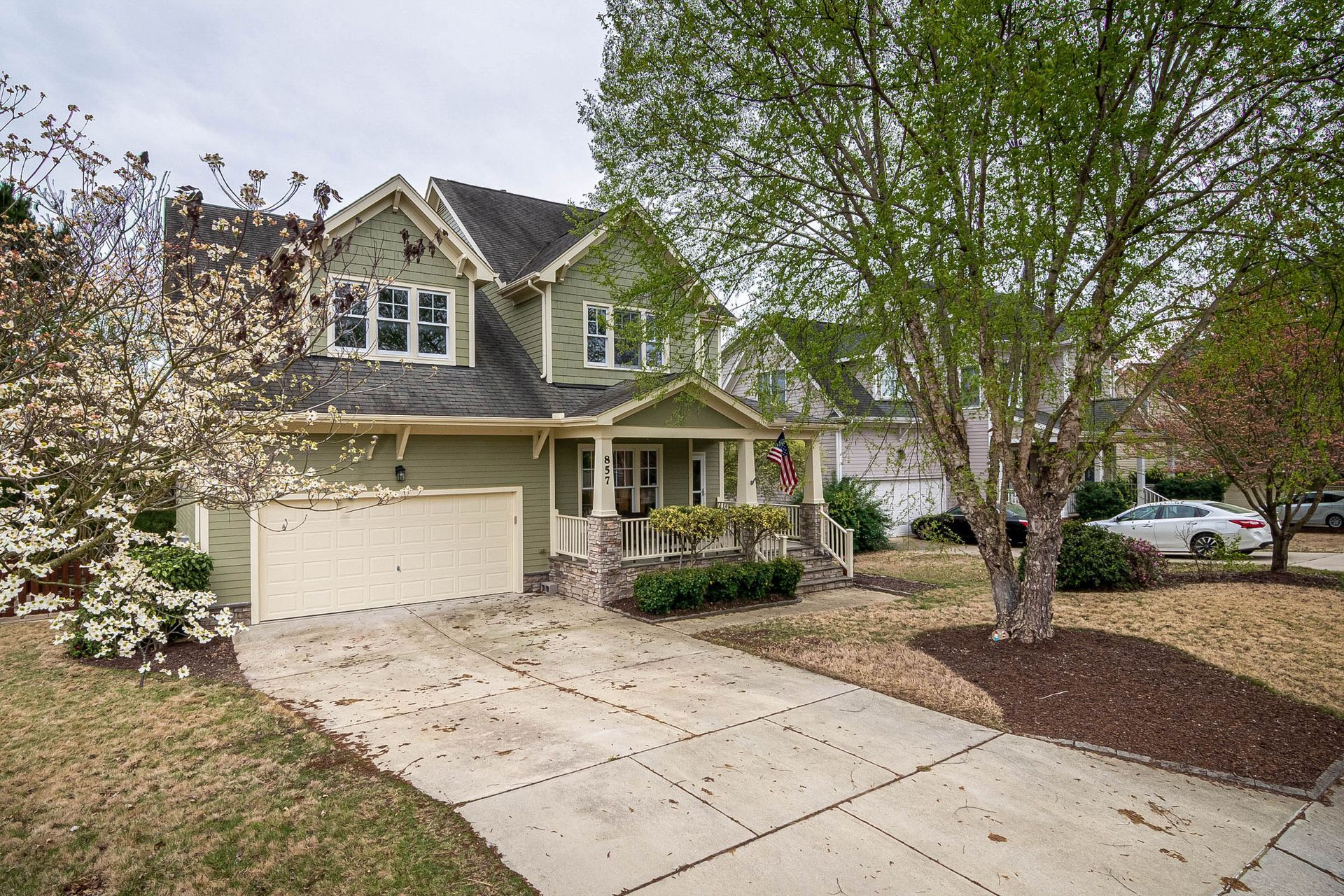 Suburban two-story house with a beige garage, front porch, and driveway lined by trees.