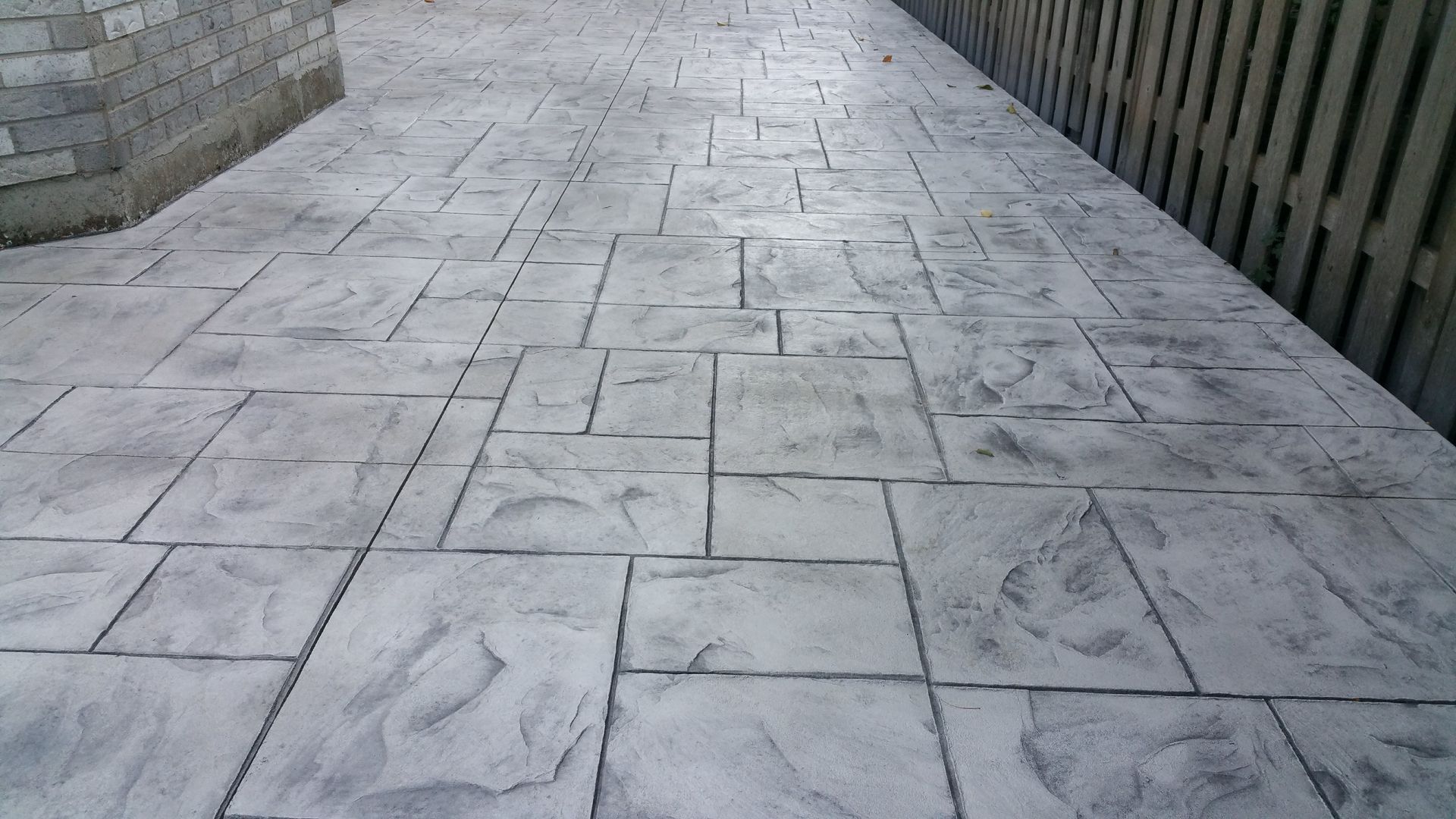 A concrete walkway with a wooden fence in the background.