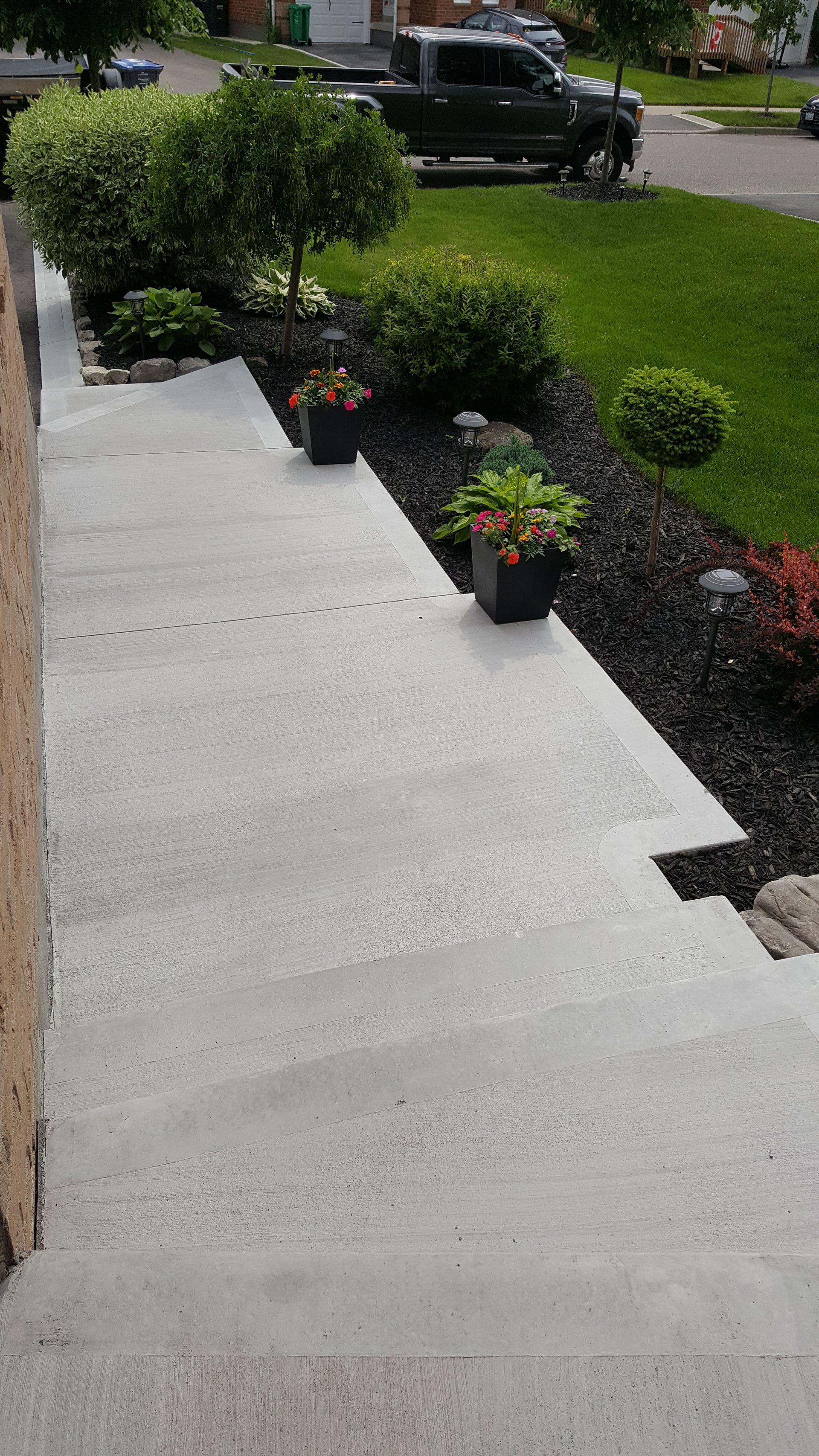 A concrete walkway with potted plants and a truck parked in the background.