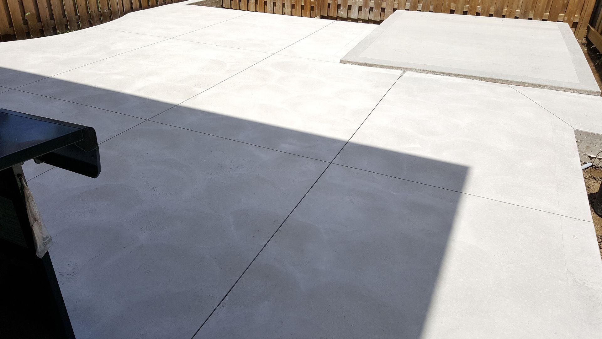 A white concrete patio with a wooden fence in the background.